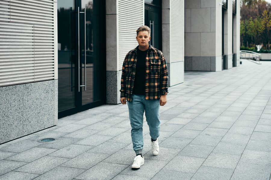 Full-body shot of a man walking down a street, one foot ahead, looking past the camera