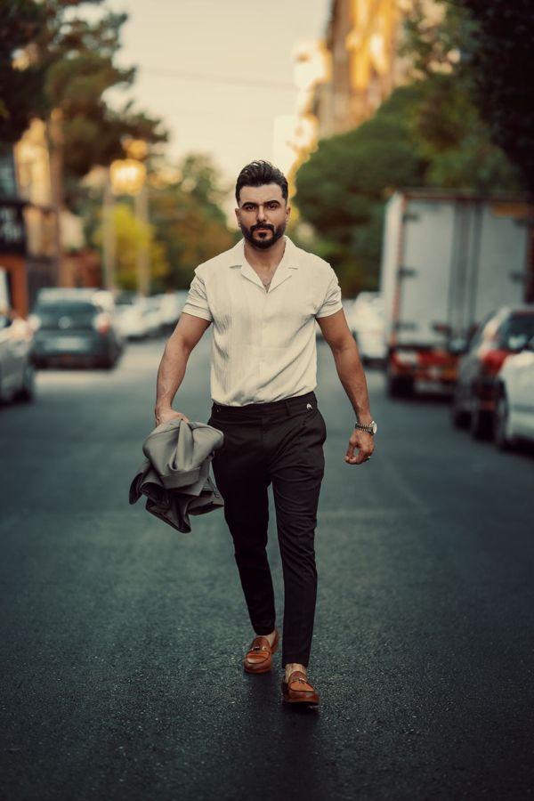 Man walking toward the camera on a street holding a jacket, mid-stride