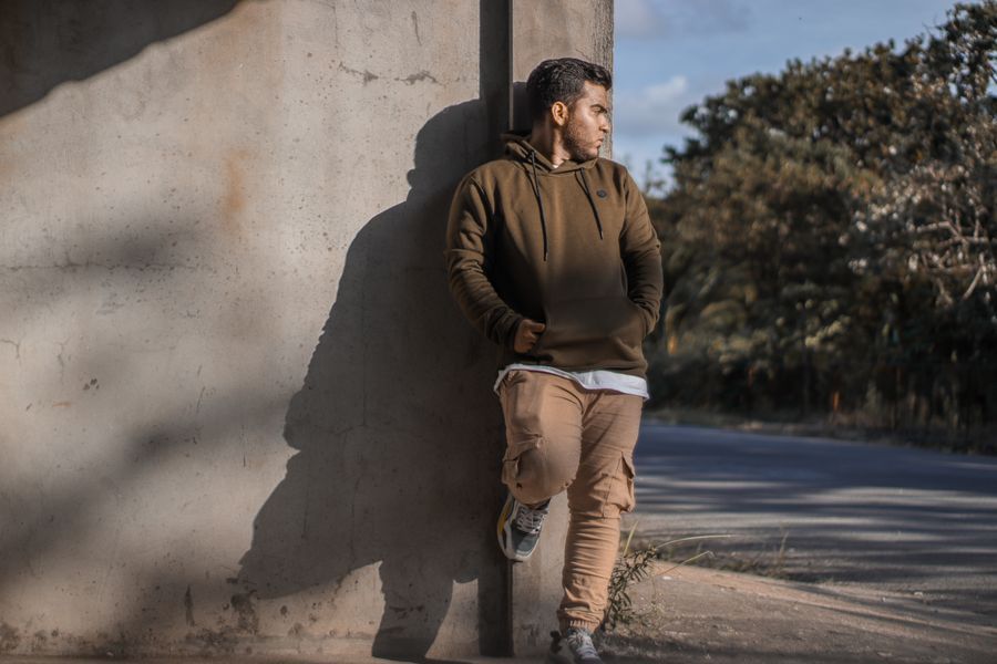 Man leaning one shoulder against a wall with hands in pockets, looking away
